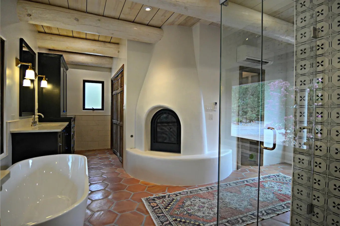 Bathroom with freestanding tub, kiva fireplace, glass shower and saltillo floor