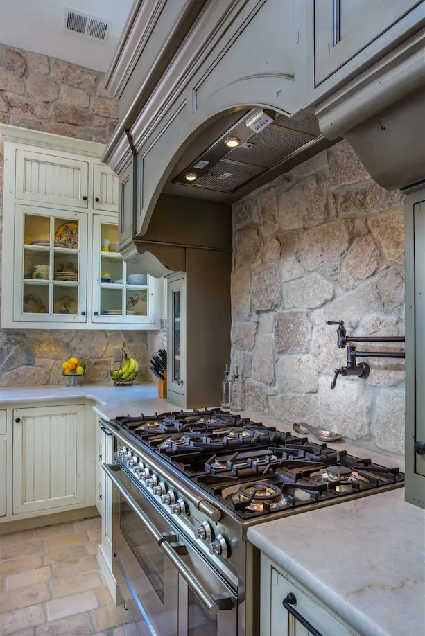 Kitchen with gas range, pot filler, stone backsplash and cream cabinets
